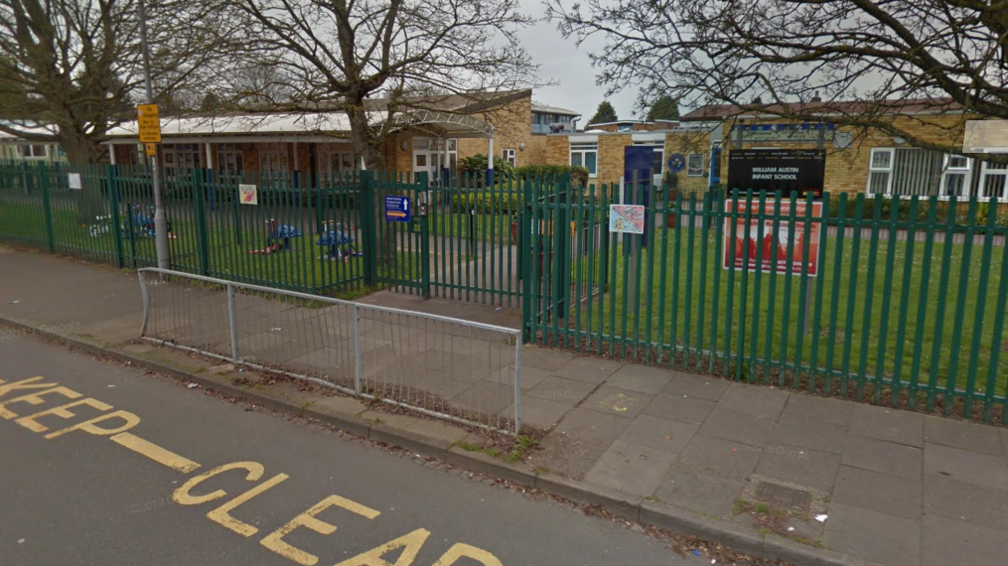 The entrance of an infant school with railings, pavement and road with a "keep clear" painted on the road outside.