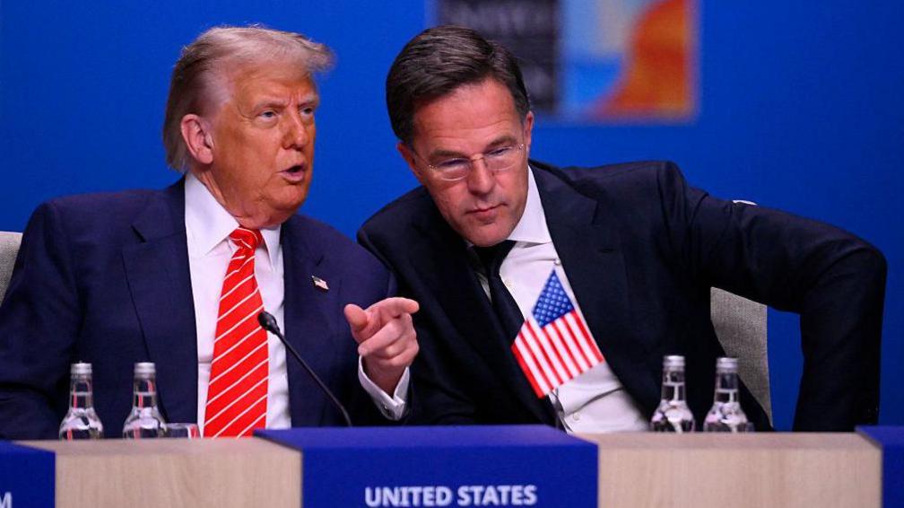 US President Donald Trump (L) in a blue suit speaks to NATO Secretary General Mark Rutte in a darker suit and leaning towards him at the start of a NATO leaders summit in The Hague,