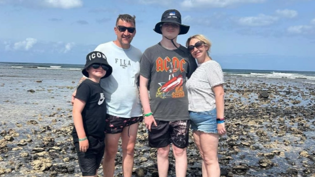 Hector and his family on holiday. They are standing on a rocky beach with the sea behind them