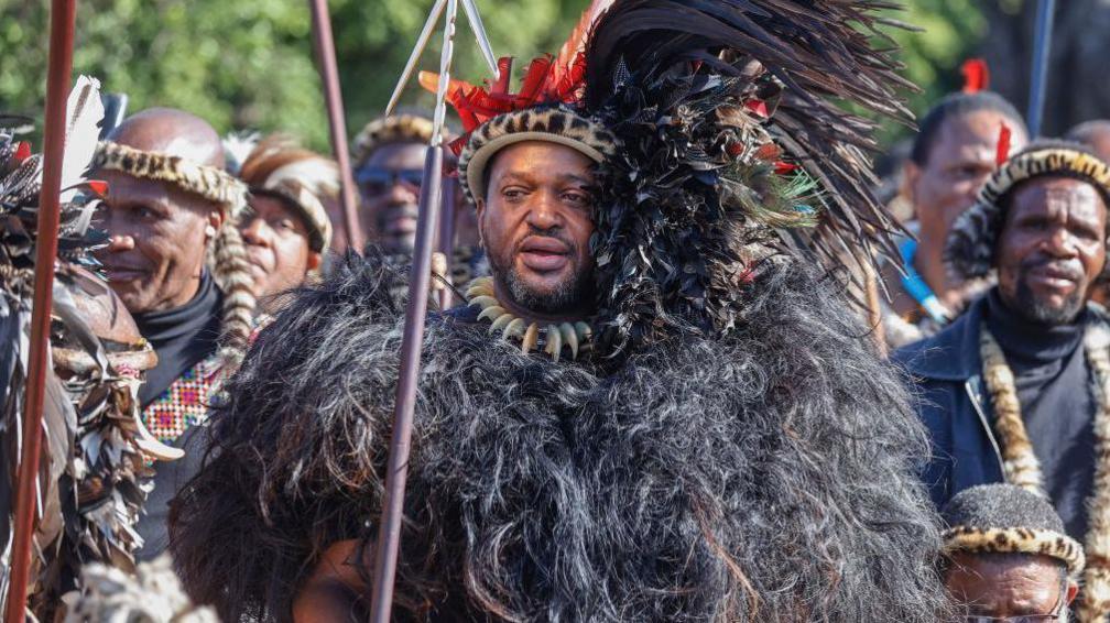 Misuzulu kaZwelithini (C) in black feathered dress and holding a spear is surrounded by men in the dress of Zulu regiments during his traditional coronation at the KwaKhangelamankengane Royal Palace on 20 August 2022.