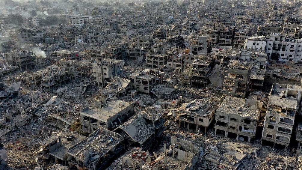 An aerial shot shows vast destruction: bombed out buildings, rubble, and rising smoke. 
