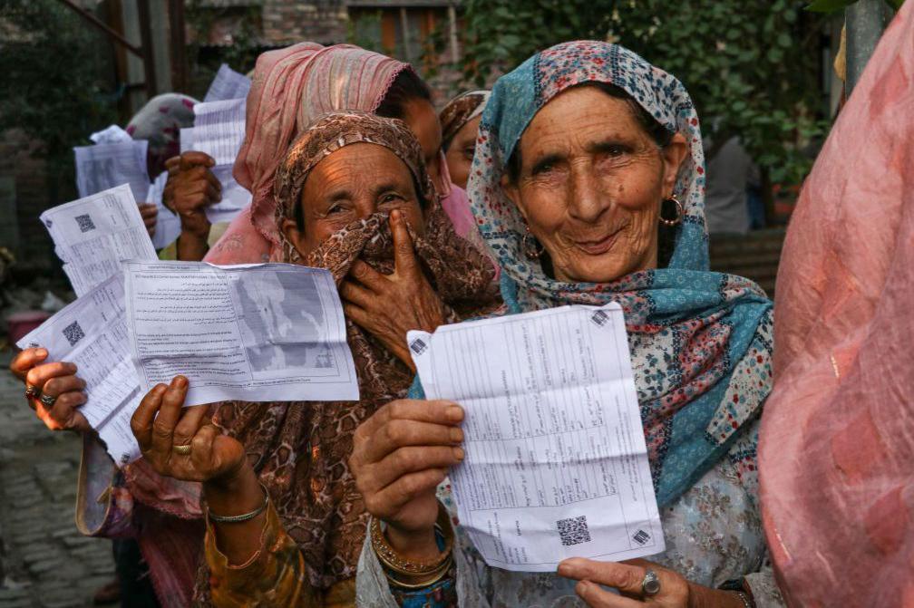 People display their voting cards as they wait in line to cast their votes at a polling station during the second phase of assembly elections in Srinagar, Indian Administered Kashmir, on September 25, 2024. 