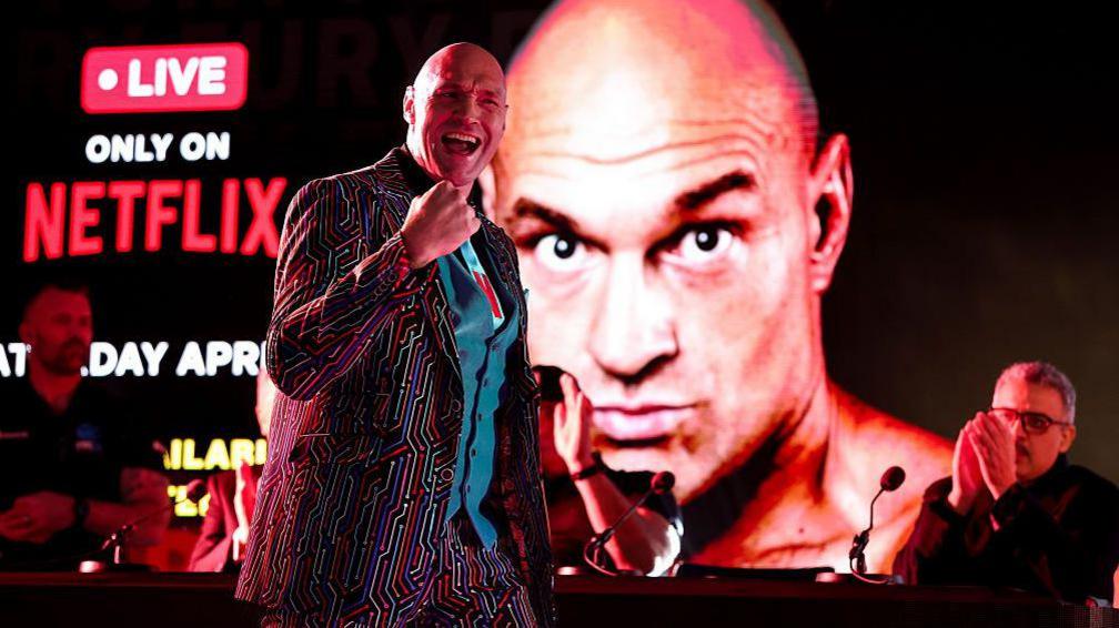 Tyson Fury making his entrance at a news conference in London, with Netflix branding behind him