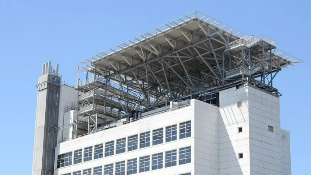 A close up image of the top of a white tower block with a square helipad structure on top