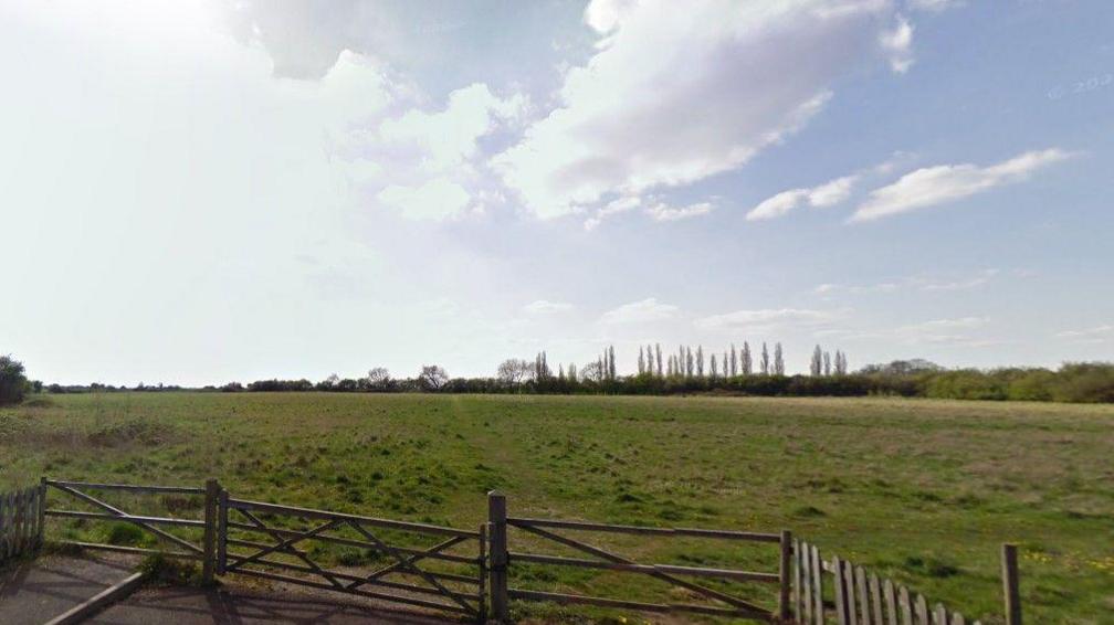 Gates in front of open fields, with trees in the distance and blue sky above.