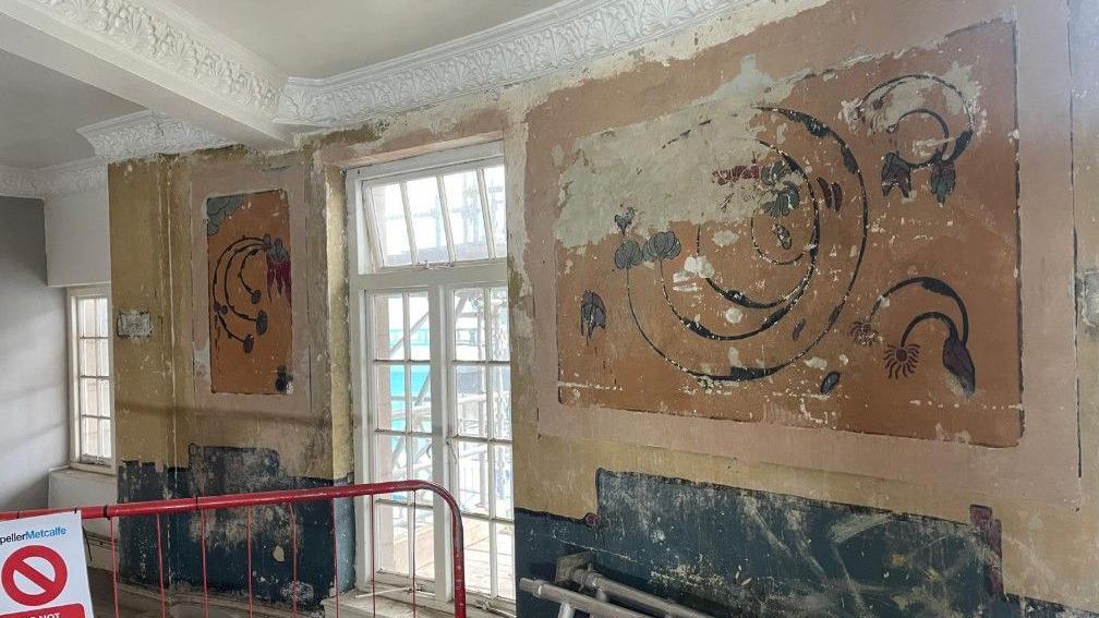 Two frescos are visible - they are either side of two glass doors. A red barrier is near the doors and silver beams are next to the wall.