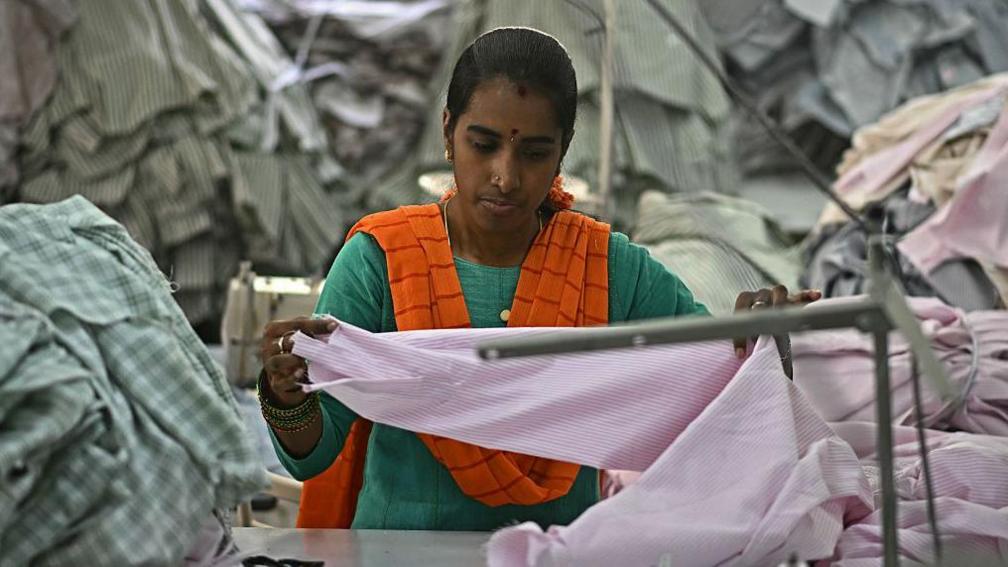 A garment worker wearing a green dress and saffron scarf sorts tailored shirts at an apparel manufacturing unit in Bengaluru on August 25, 2025.