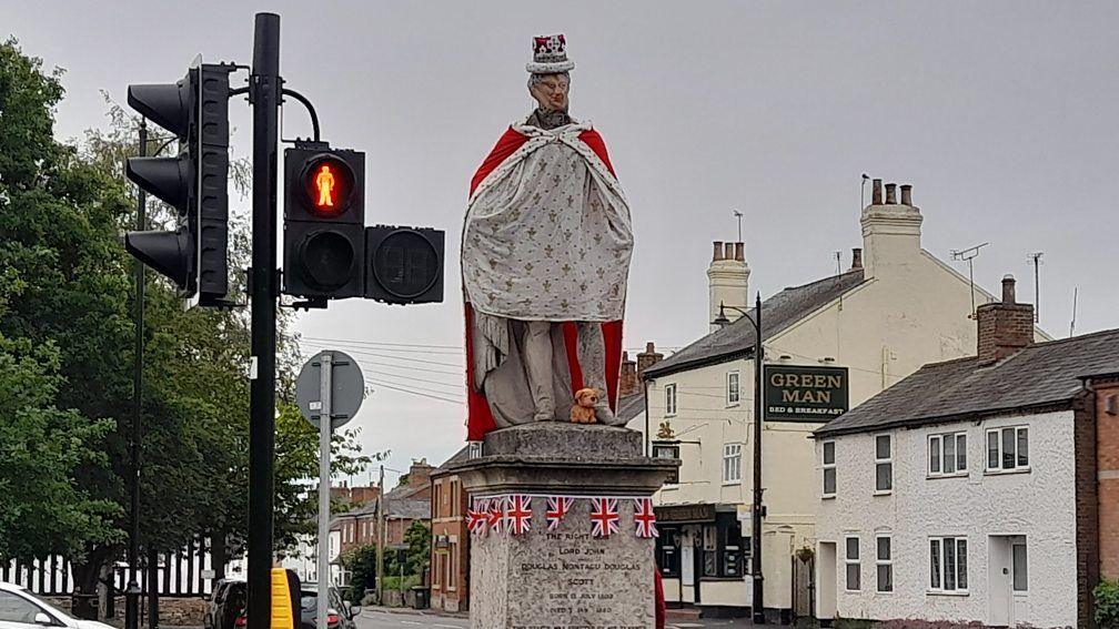 Statue with royal robes, a depiction of the late Queen's face and the state crown on top. A string of union jacks have been placed round the plinth of the statue. 