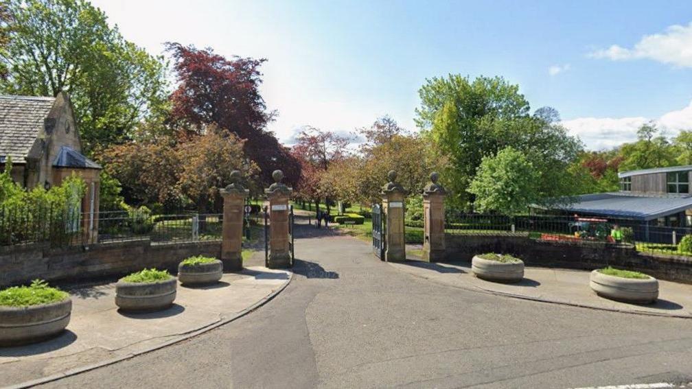 Stone gates mark the entrance to the park. There are trees in the background. 