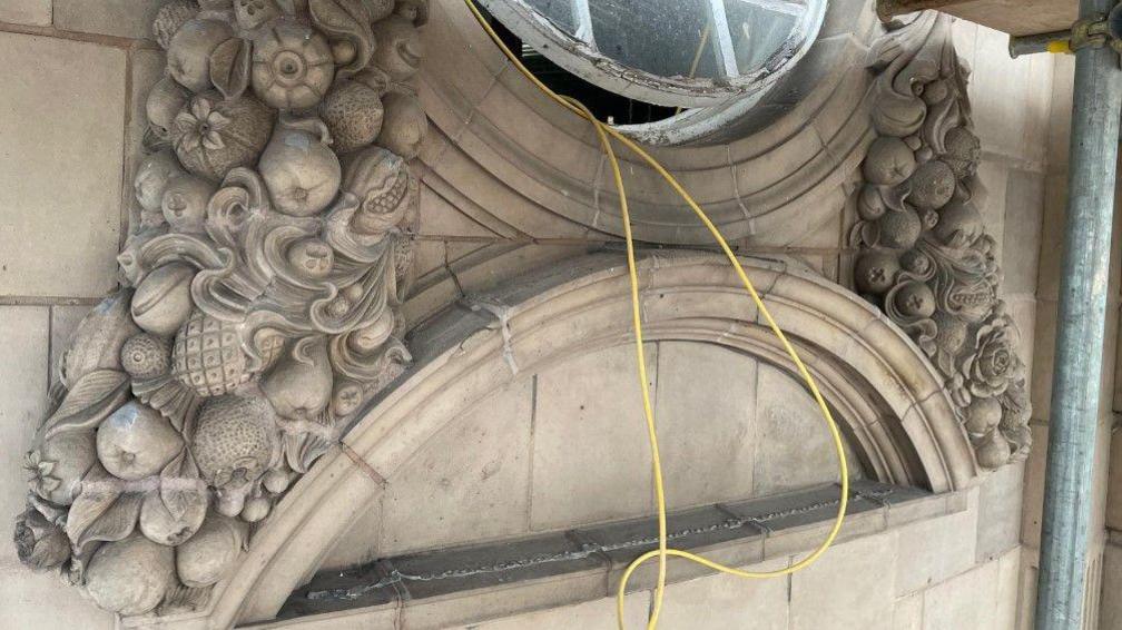 An ornate wall, including a partially open window. A yellow wire is coming down from the gap in the window. 