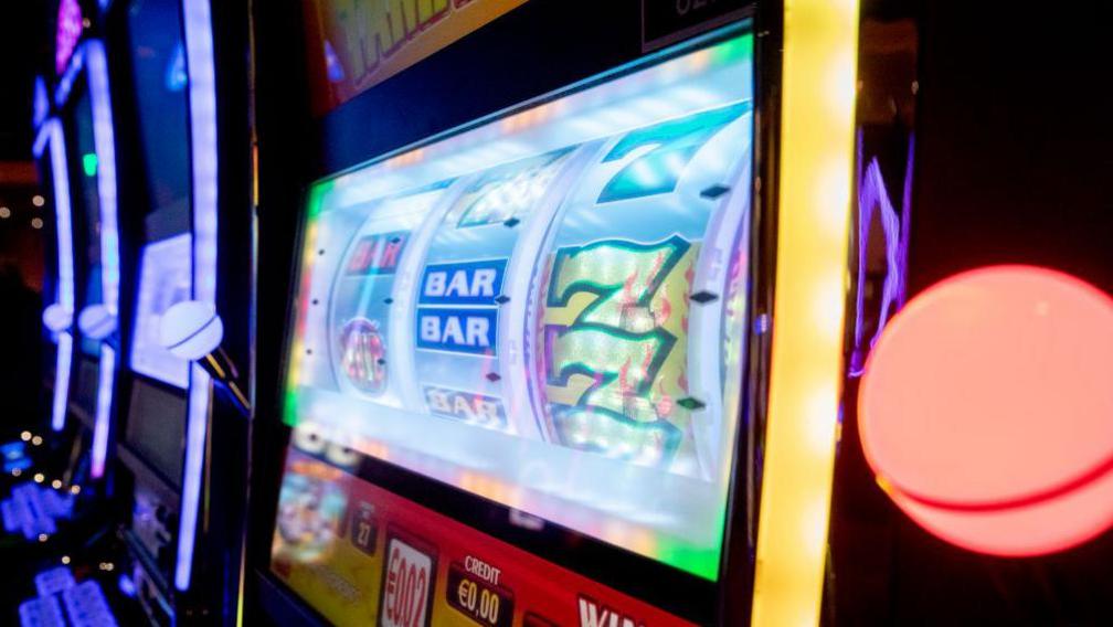 We can see the screen of a digital slot machine. It's displaying a traditional style game with three reels where we can see the number 7 and 'Bar'.