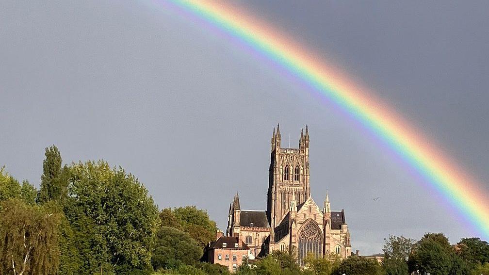 A rainbow streaks across the sky with red, yellow, green and purple shades over the square spire of a cathedral.