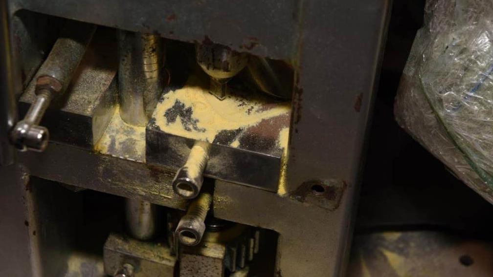 A metal pill pressing machine with traces of white/yellow powder on some of the surfaces