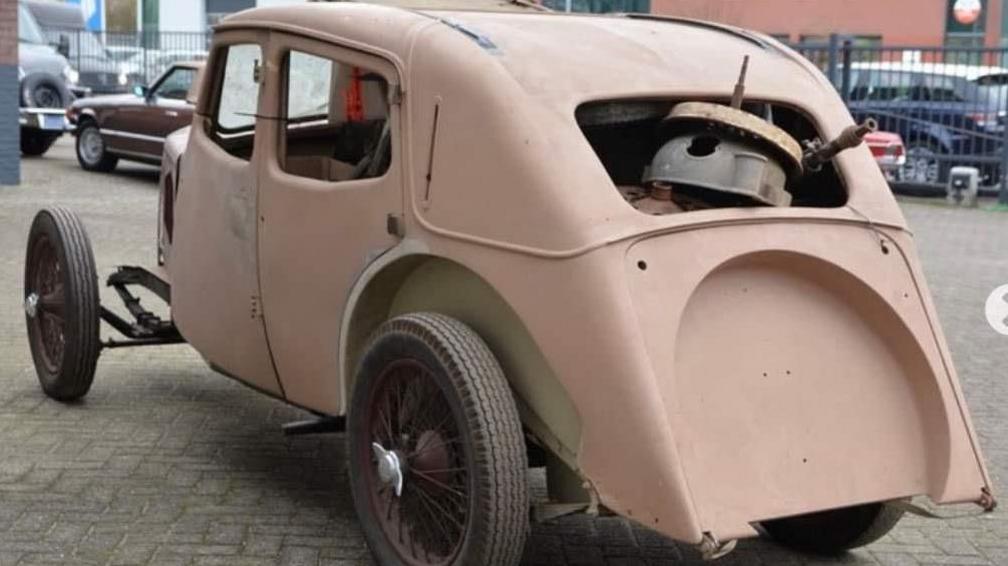 Delapidated pink car with spare wheel missing and various parts visible through the back window