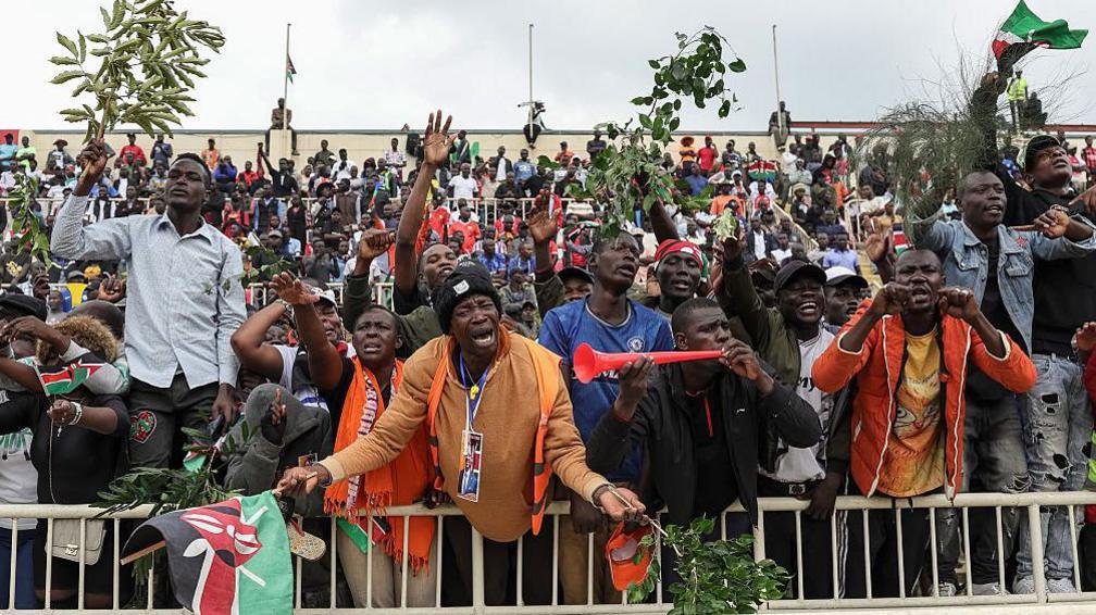 Mourners carrying Kenyan flags and branches at Nyayo stadium 