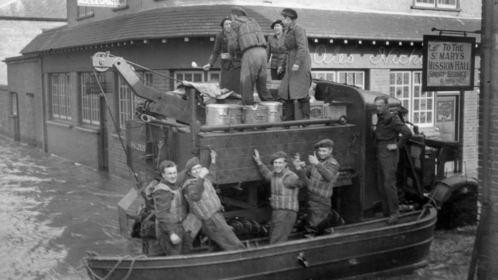 Four men standing in a boat taking supplies from a lorry in Maidenhead during the floods in 1947