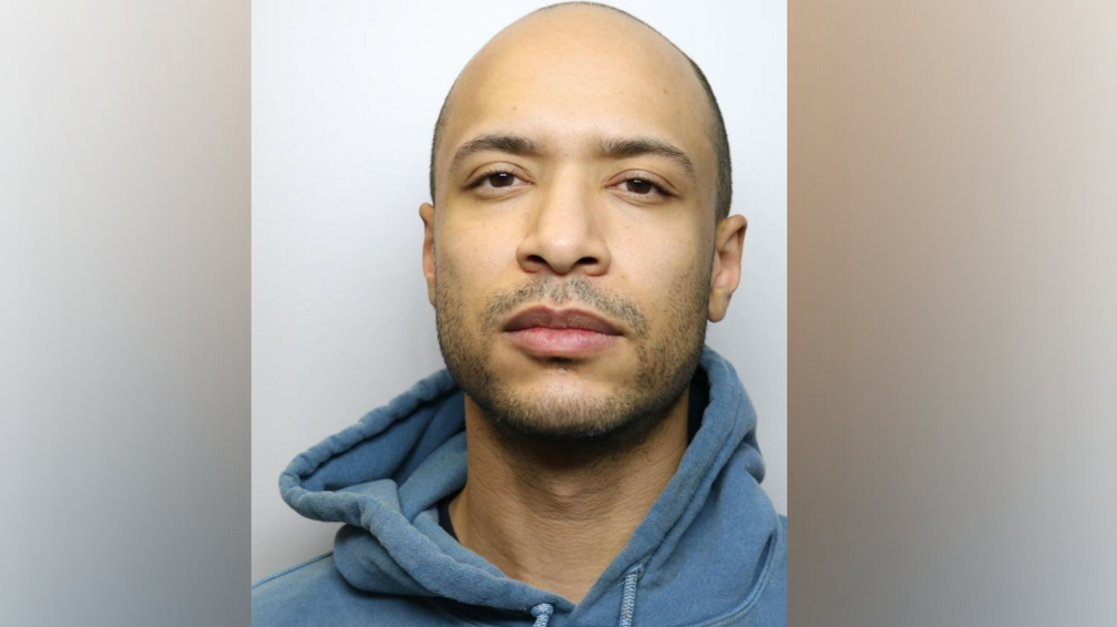 A police mugshot of Leo Faradoye. He is balding and has a light beard and moustache and is wearing a blue hooded sweatshirt. 