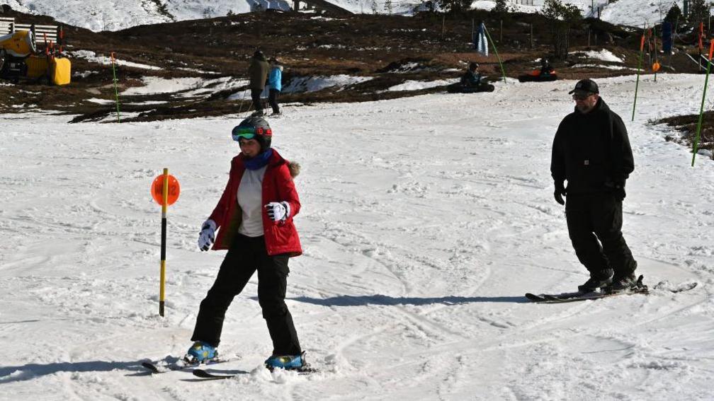 Two people ski down a snow-covered ski slope