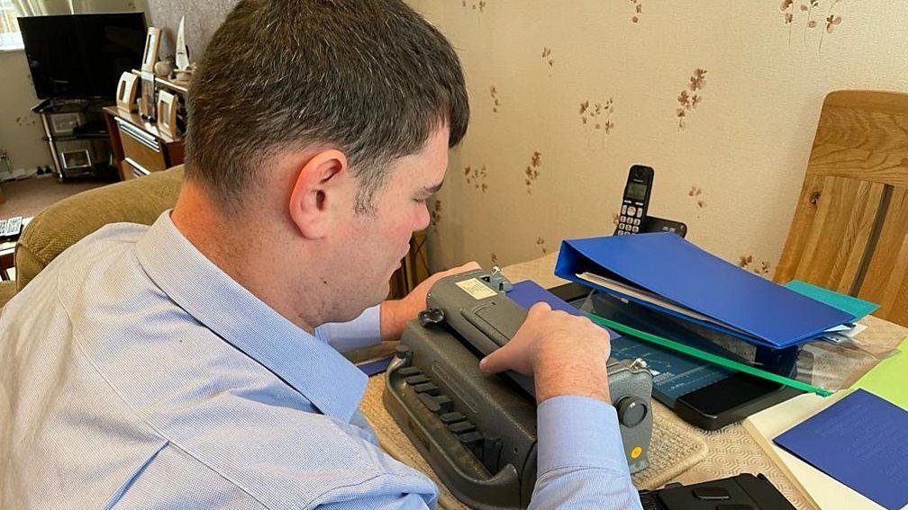 A man sitting at a desk in front of a braille typewriter