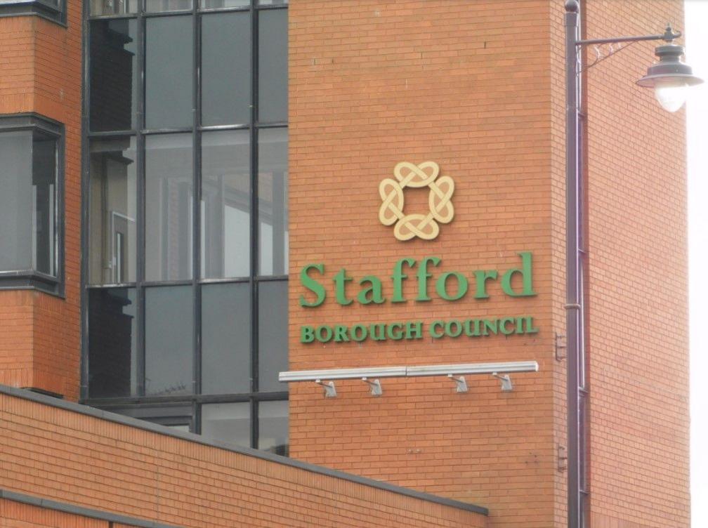 The outside of a brick building with windows on the left and the words Stafford Borough Council in green on the building in the centre and right of the photo.