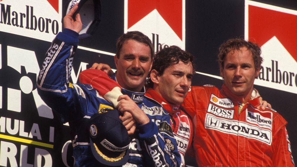 Nigel Mansell lifts his right arm in celebration after winning the 1992 F1 world championship at the Hungarian Grand Prix. Ayrton Senna has his right arm around him on the podium, and Gerhard Berger is on the far right