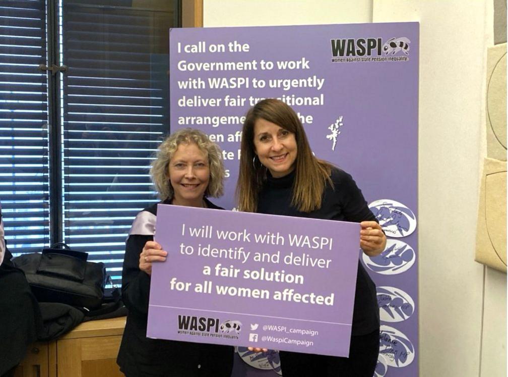 Liz Kendall holds a purple placard reading: I will work with WASPI to identify and deliver a fair solution for all women affected. She is standing alongside a female campaigner in front of a sign promoting the Waspi women campaign.