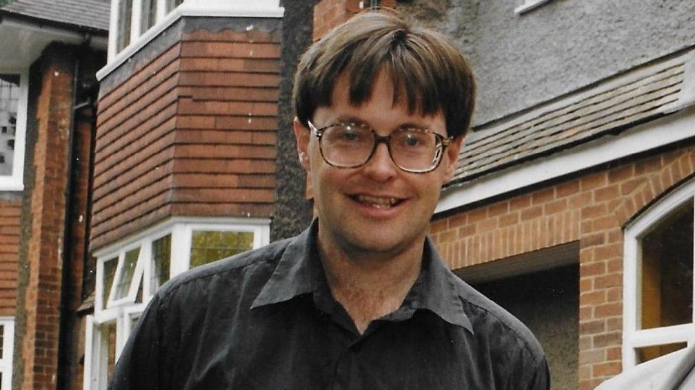 An old photograph of Andrew Redfern wearing glasses and a dark shirt