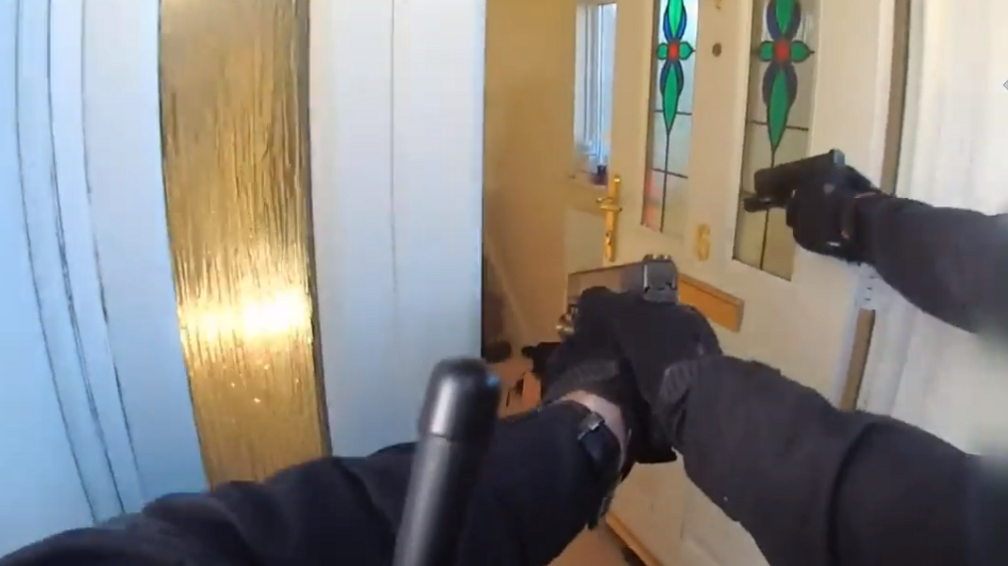 Police officers pointing a gun towards a front door