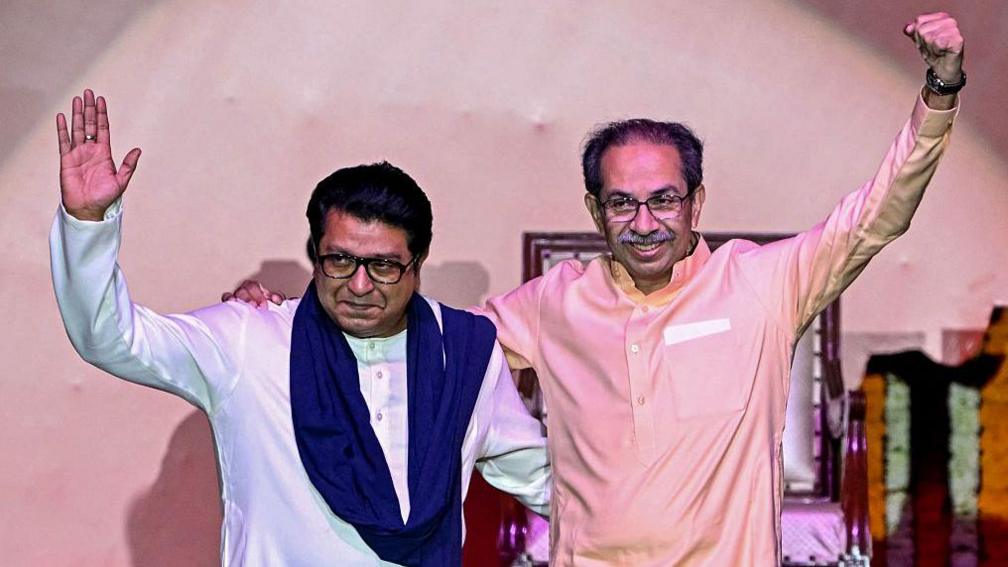 Hindu right-wing political party chief Shiv Sena (UBT) Uddhav Thackeray (R) and his cousin and Maharashtra Navnirman Sena (MNS) president Raj Thackeray gesture as they greet the crowd upon their arrival on stage to address a joint rally against the imposition of the Hindi language in primary schools, in Mumbai on July 5, 2025.