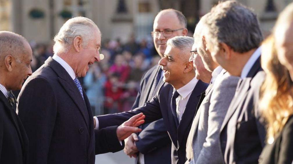 Sadiq Khan laughs as he greets the King with a handshake. He is in a line up of people waiting to meet the King. 