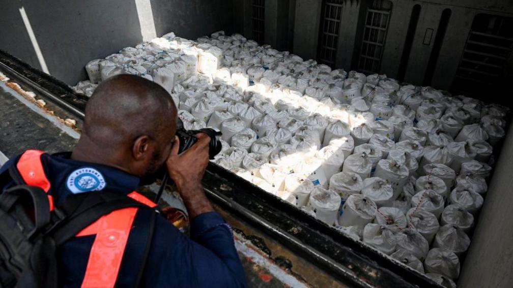 A photojournalist takes a photo of white sacks containing ammonium nitrate.