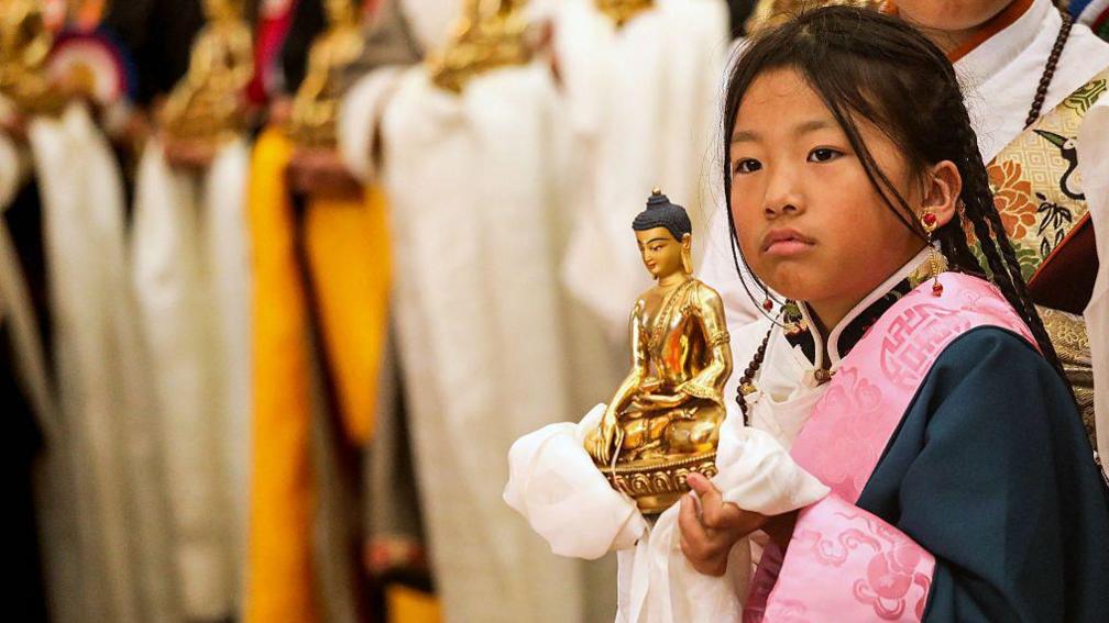 A Buddhist devotee holds a golden Buddha figurine as she waits for the arrival of Tibetan spiritual leader the Dalai Lama, before the start of a Long Life Prayer offering ceremony at the Main Tibetan Temple in McLeod Ganj, near Dharamsala on June 30, 2025. (Photo by Sanjay BAID / AFP) (Photo by SANJAY BAID/AFP via Getty Images)