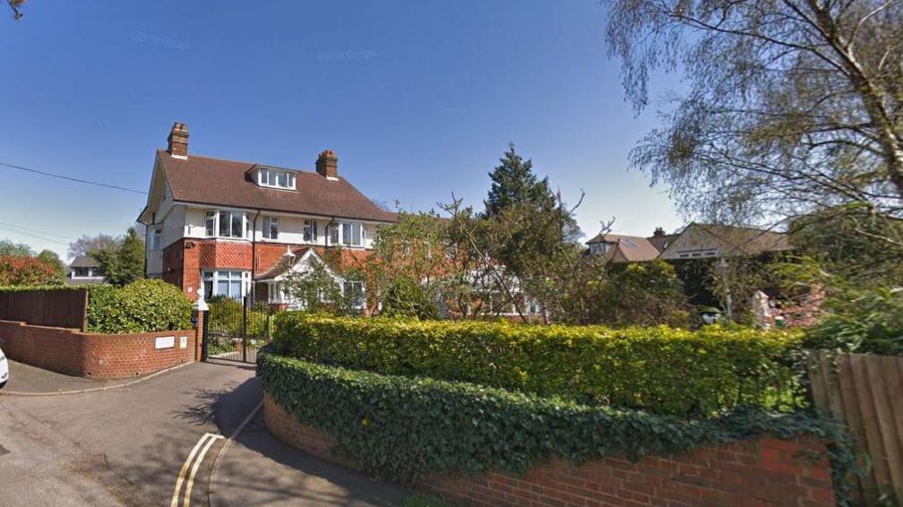 The outside of The Red House care home in Ashtead which is behind a hedge and has a high black metal gate in front of it