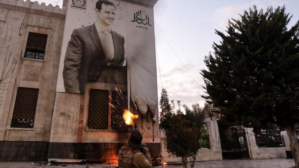 A fighter firing at a poster of Assad