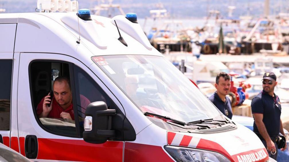 An ambulance is parked near the harbor where a search continues for missing passengers after a yacht capsized on August 19, 2024