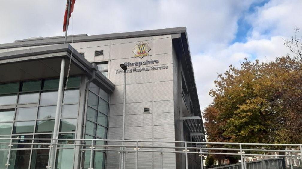 A building with a flag above it. The words Shropshire Fire and Rescue Service are on the building and a tree is on the right of the photo.