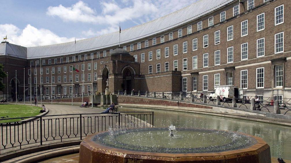 The front of the City Hall building with the fountain on, on a sunny day