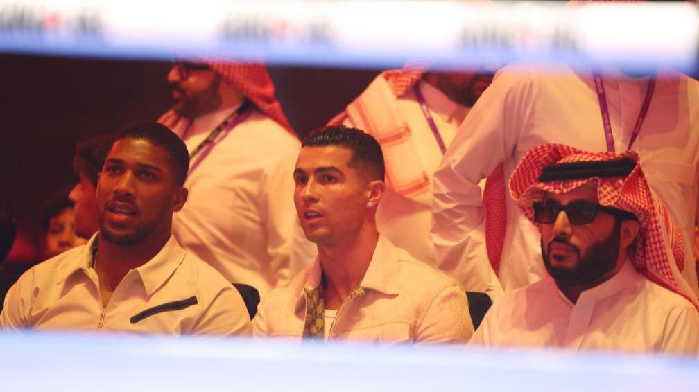 Anthony Joshua and Cristiano Ronaldo sit alongside Turki Alalshikh as they watch a fight from ringside