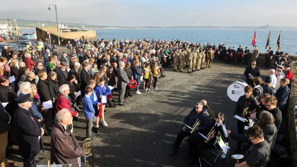 A large crowd gather at a war memorial by the sea in Penzance for a remembrance service in the town.