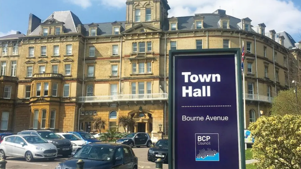A sign says Town Hall and carries the BCP Council logo. Behind it is the five-storey Bournemouth Town Hall, a historical building in light-brown stone with large buildings.