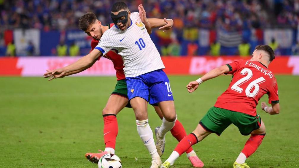 Kylian Mbappe of France holds off Ruben Dias of Portugal as he is tackled by Francisco Conceicao of Portugal 