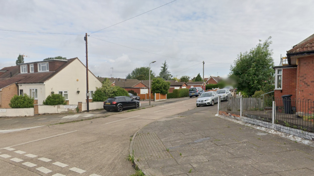 View looking down Radiant Road from a neighbouring street with cars parked along it and homes of various sizes visible