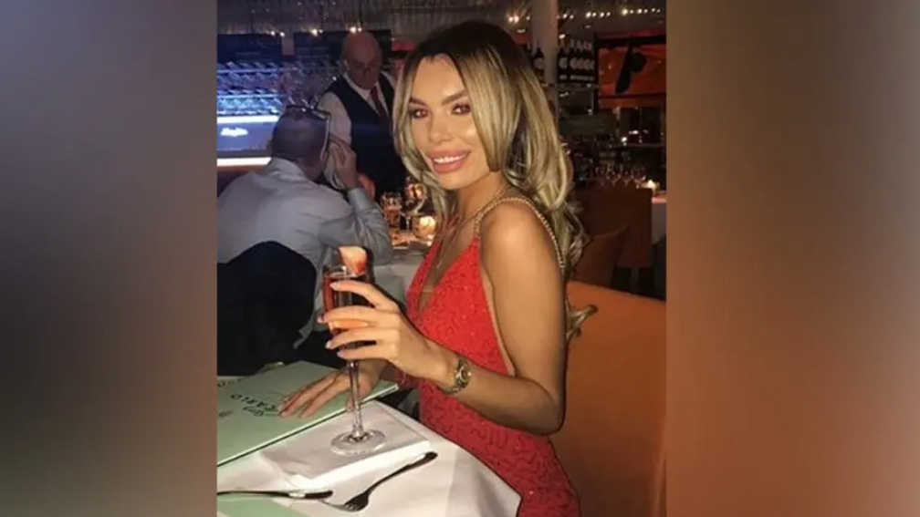 Ashley Dale, wearing a red dress, smiles as she raises a glass in a toast during a night out at a restaurant