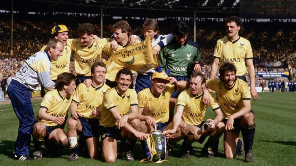Oxford United's team in yellow shirts and blue shorts line up at Wembley with the Milk Cup Trophy after beating QPR
