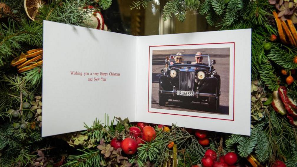 Prince Charles's Christmas card from 2019, featuring the prince driving a classic sports car, with Camilla sitting in the front passenger seat. The message says: Wishing you a very Happy Christmas and New Year.