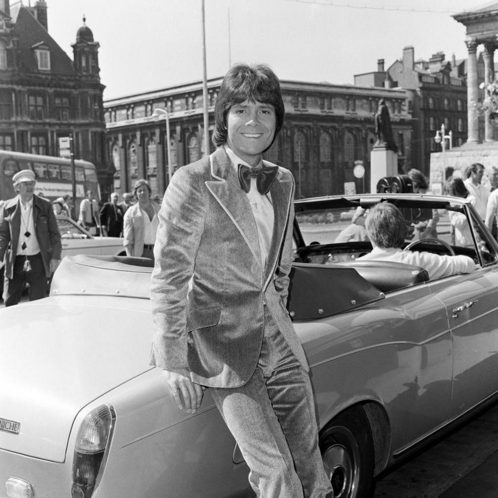 A black and white image of a smiling Cliff Richard leaning on an open top car in Birmingham's Victoria Square
