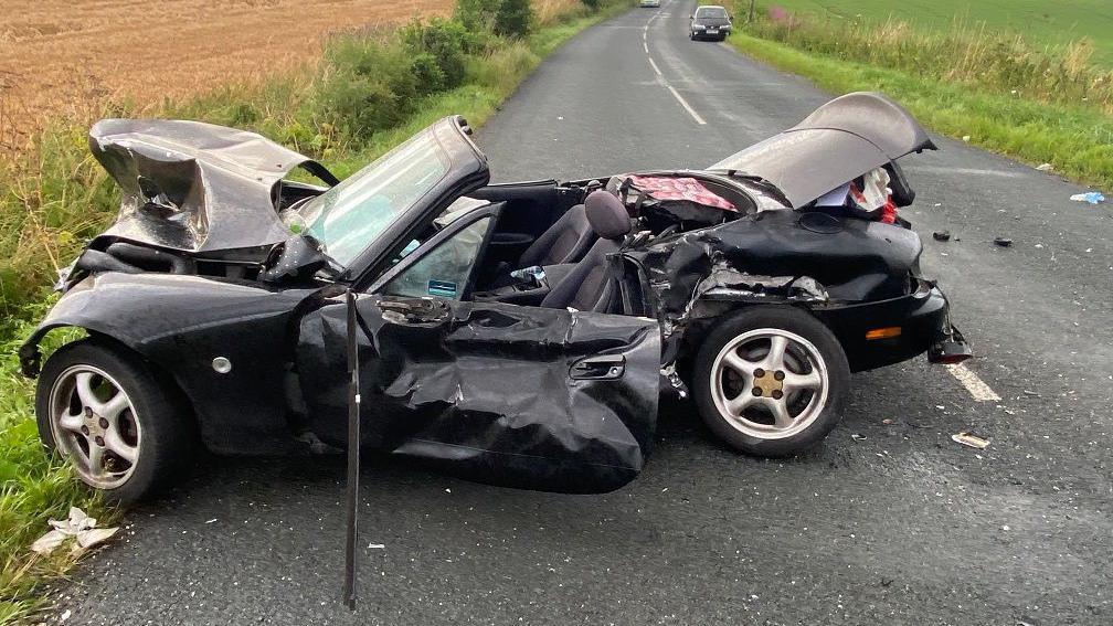 A crumpled black Mazda MX5 on the road