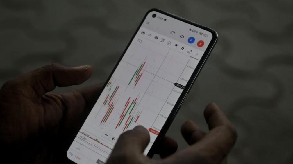 A man (not pictured) browses a stock market app showing technical charts.