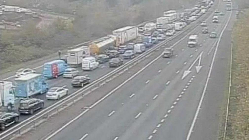 A picture of standstill traffic on one side of a motorway carriageway; traffic on the opposite carriageway runs freely.