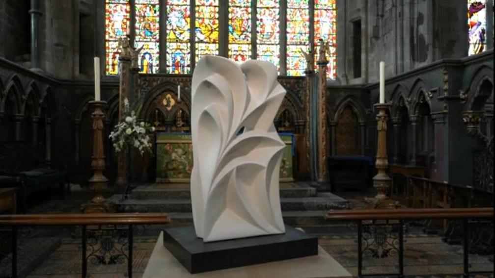 A large white sculpture sits in front of the altar and stained glass window of a church